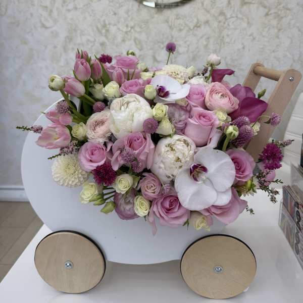 Pastel pink and white flower arrangement in a small white wooden cart with wheels.