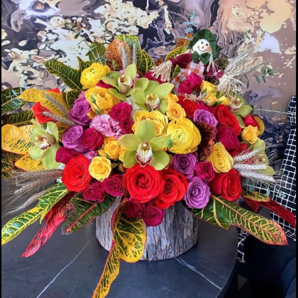 Colorful bouquet of roses and orchids in a wood container with a scarecrow pick