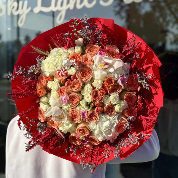 Large bouquet of peach and white roses wrapped in bright red paper