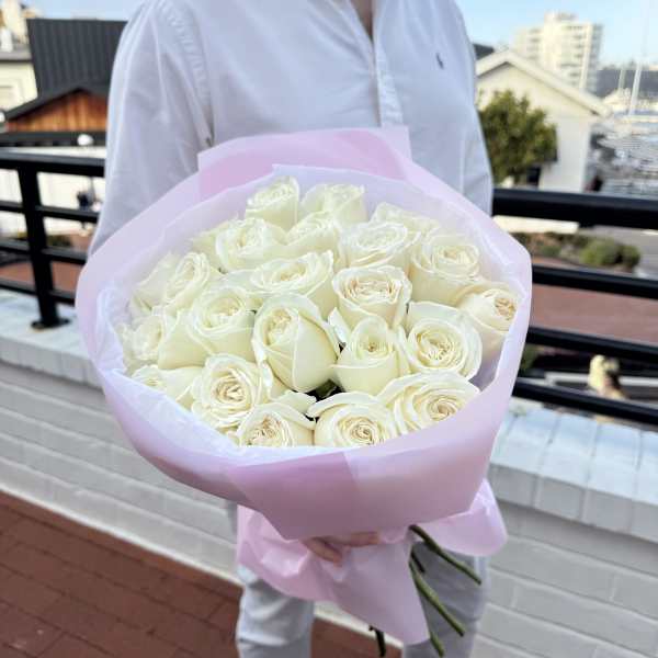 Large bouquet of cream roses wrapped in pale pink paper held by a person in a white shirt.