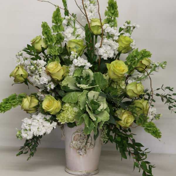 Tall arrangement of green roses, white stock, and Bells of Ireland in a cream ceramic vase