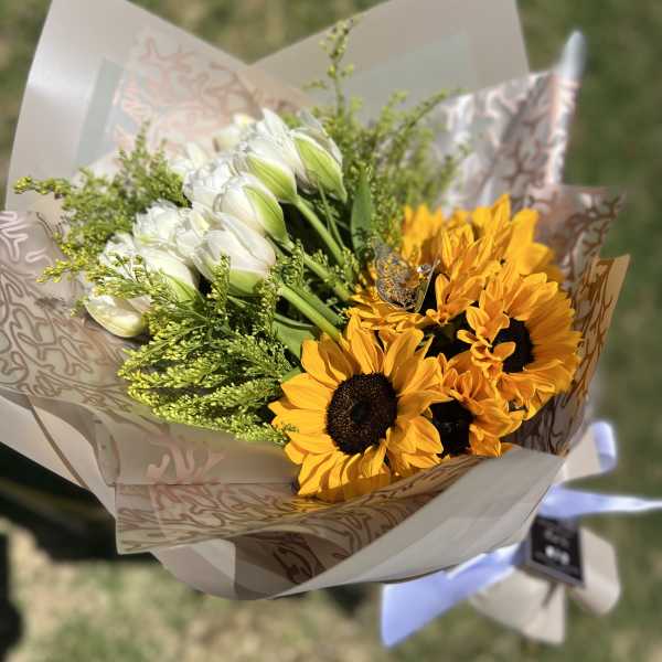 Bouquet of white tulips and yellow sunflowers in patterned wrap