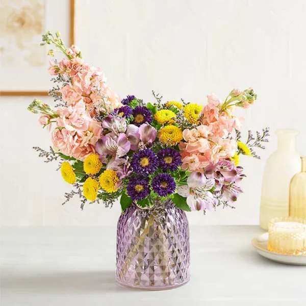 Mixed bouquet in a purple glass vase with pink, yellow, and purple flowers