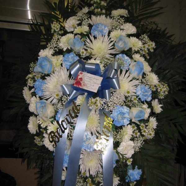 Standing sympathy wreath with white mums and blue roses on an easel with blue ribbons
