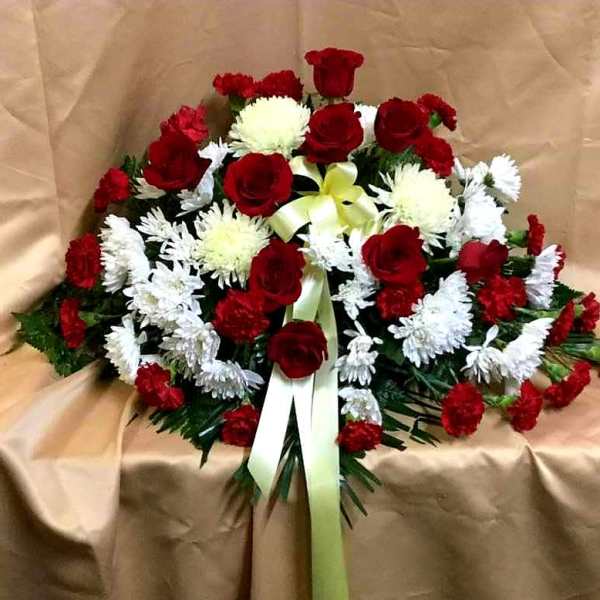 Red roses and white chrysanthemums arranged with a pale ribbon on tan fabric
