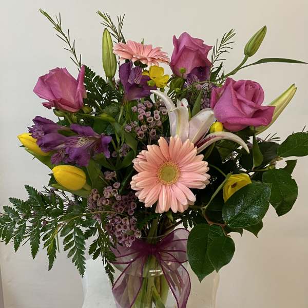 Mixed bouquet with pink roses, lilies, tulips, and a gerbera daisy in a glass vase
