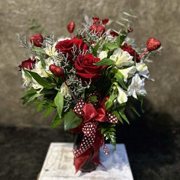 Red roses and white flowers in a vase with heart picks and ribbon