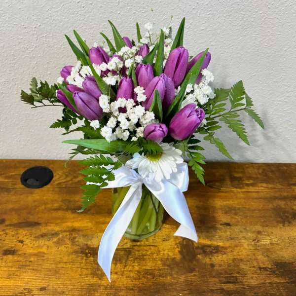 Purple tulips and white daisies in a glass vase with a white ribbon