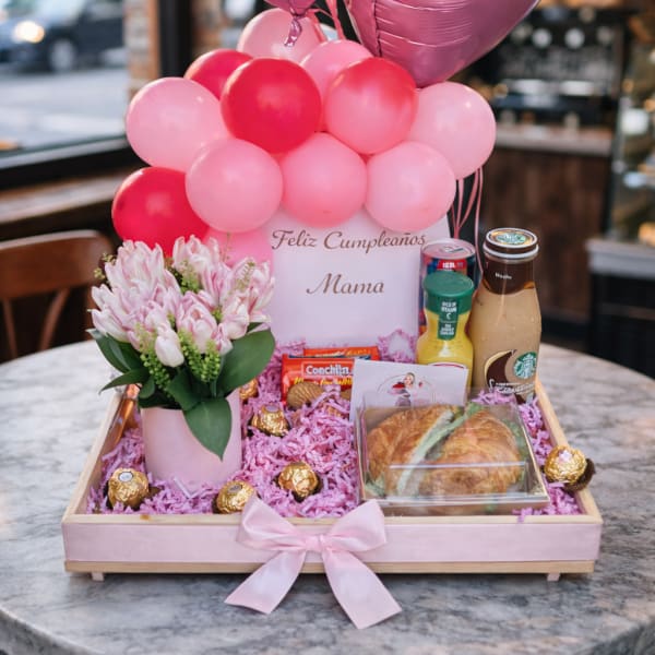 Pink balloon gift tray with flowers, chocolates, pastries, and drinks