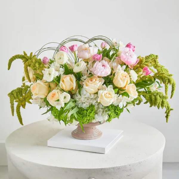 Pastel floral arrangement in a pedestal vase with arching greenery