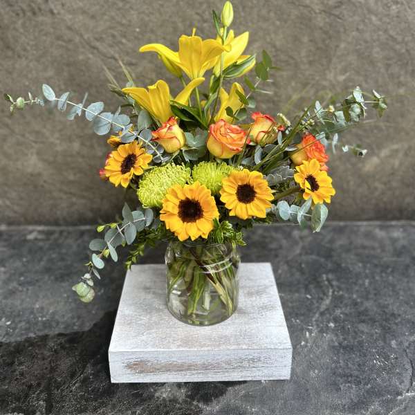 Yellow lilies and sunflowers in a glass jar vase