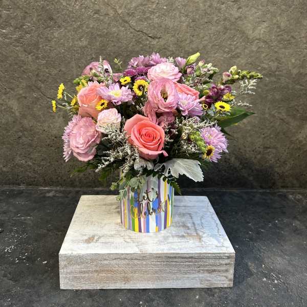 Pink and lavender mixed bouquet in a striped "let's celebrate" container
