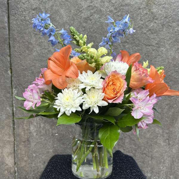 Mixed bouquet of orange, blue, pink, and white flowers in a glass vase