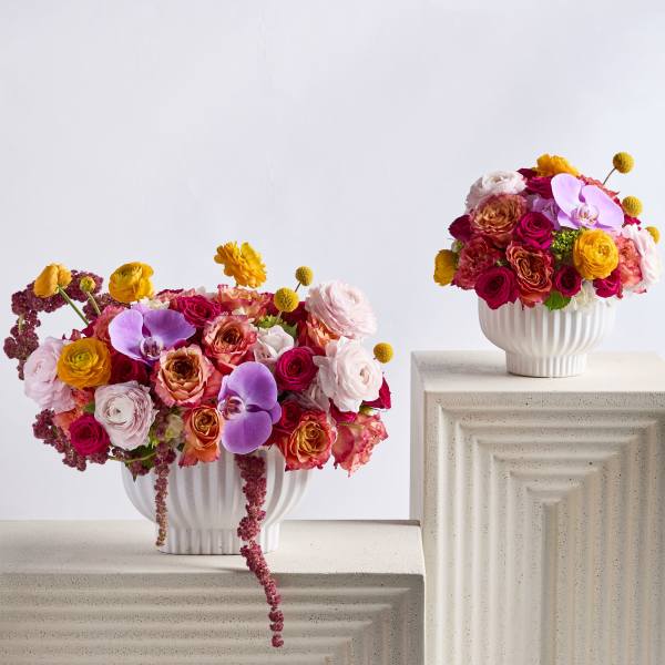 Two colorful flower arrangements in white vases on pedestal stands