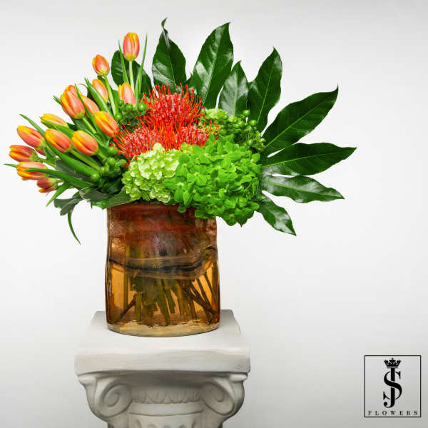 Orange tulips and red tropical flowers in an amber glass vase