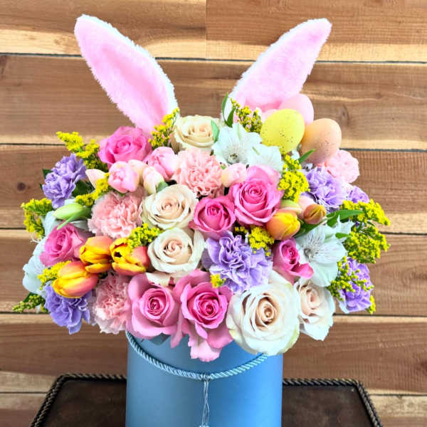 Pastel flower arrangement in a blue hatbox with pink bunny ears and decorative eggs