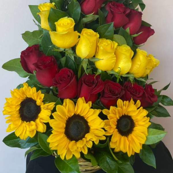 Tall arrangement of red and yellow roses with yellow sunflowers in a basket