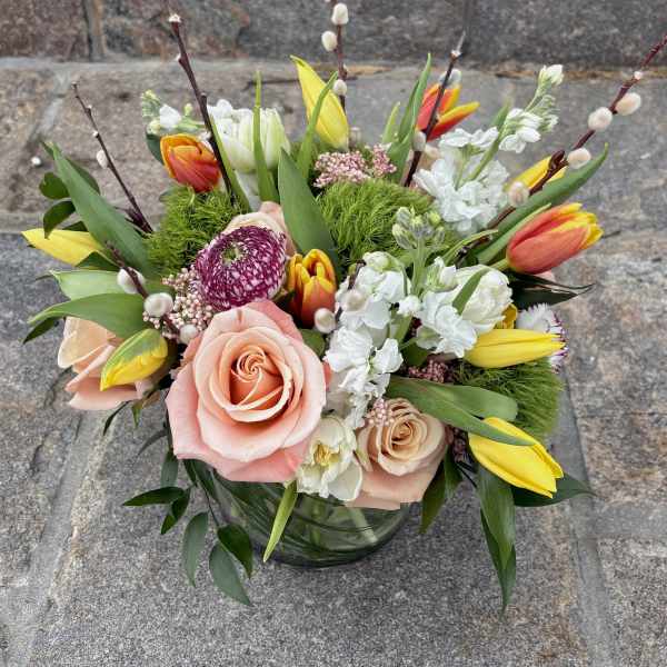 Low glass vase of peach roses, yellow and orange tulips, white blooms, and pussy willow branches