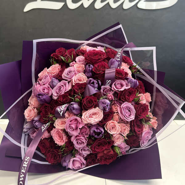 Bouquet of pink, lavender, and burgundy roses wrapped in purple paper