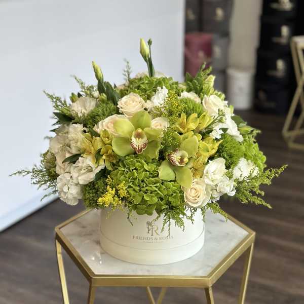 Round floral arrangement in a white hat box with white and green blooms