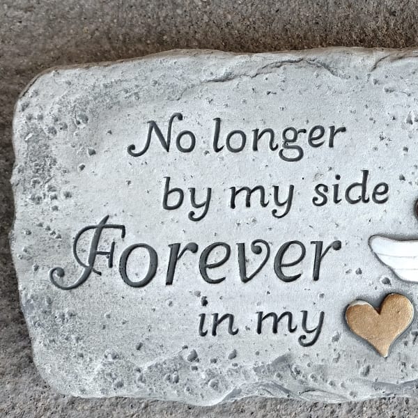 Memorial stone with paw print, halo, wings, and the words "No longer by my side Forever in my"