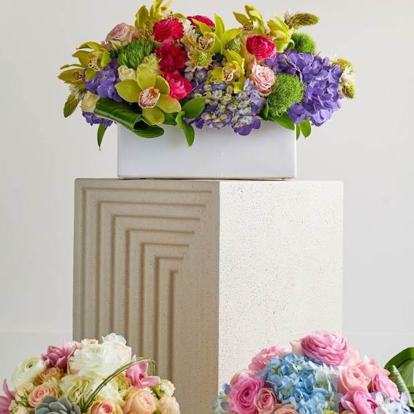 Three colorful floral arrangements on pedestals, including a purple-and-green box arrangement.