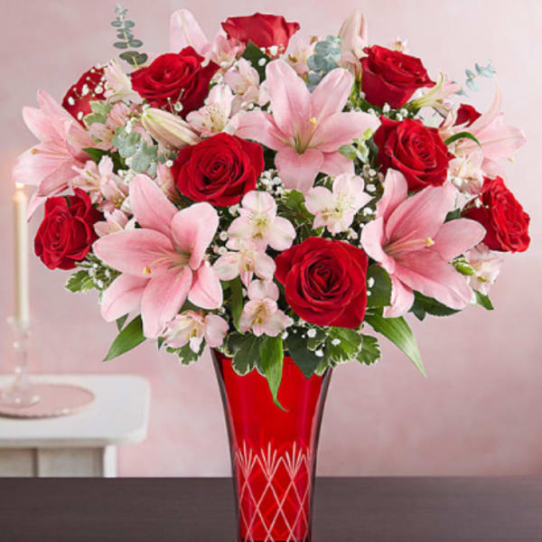 Arrangement of red roses and pink lilies in a tall red glass vase