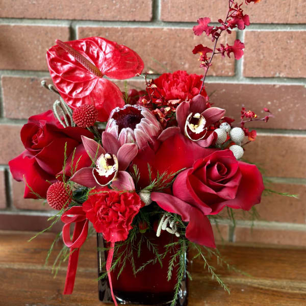 Red floral arrangement in a dark vase with roses and orchids