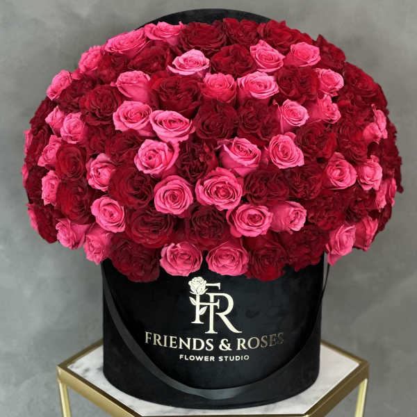 Large round arrangement of pink and red roses in a black hat box