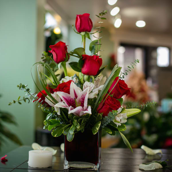 Red roses and lilies arranged in a square glass vase