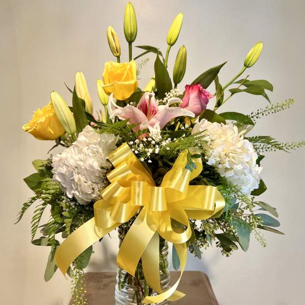 Bouquet of yellow roses, lilies, and white hydrangeas in a glass vase