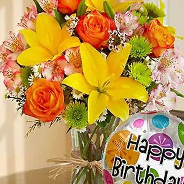Bouquet of yellow lilies and orange roses in a glass vase with a birthday balloon