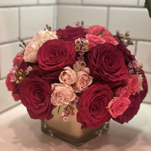 Bouquet of red and blush roses in a square glass vase