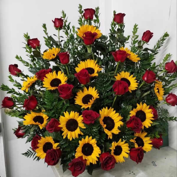 Tall arrangement of yellow sunflowers and red roses in a fan shape with lush dark green foliage