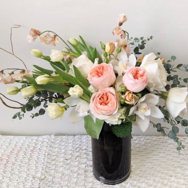 Bouquet of blush roses and white orchids in a dark vase