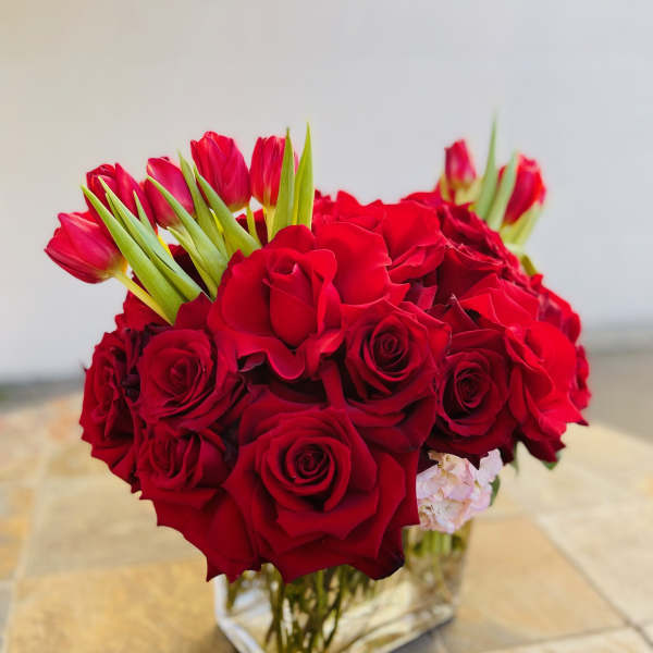 Red roses and pink tulips arranged in a clear square vase