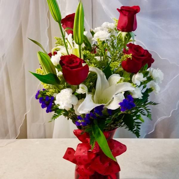 Red roses and white lilies in a red glass vase with a ribbon