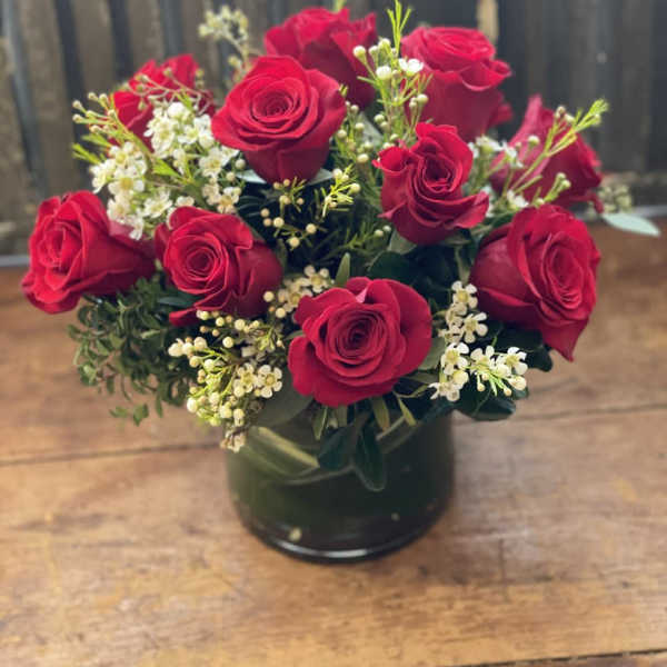 Red roses arranged in a dark glass vase with small white filler flowers