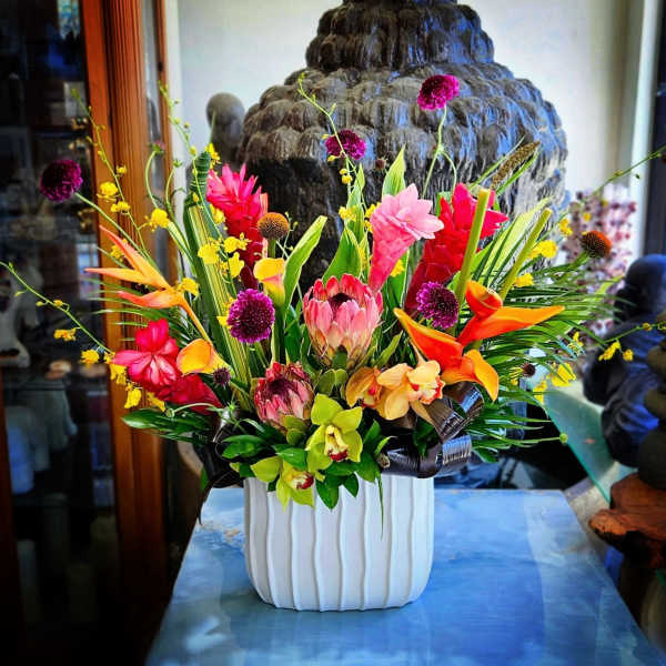 Tropical flower arrangement in a white vase with pink, orange, and yellow blooms