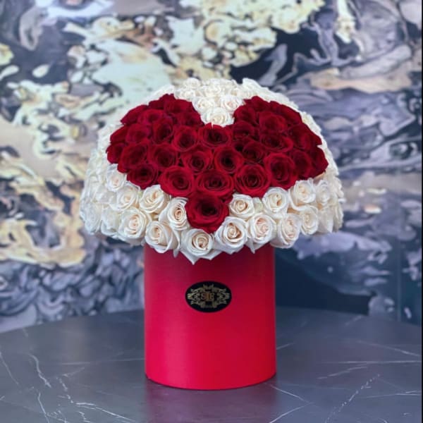 Heart-shaped red and white rose arrangement in a red cylindrical box