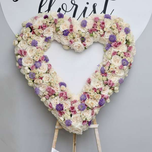 Heart-shaped floral wreath of cream, pink, and purple blooms on an easel