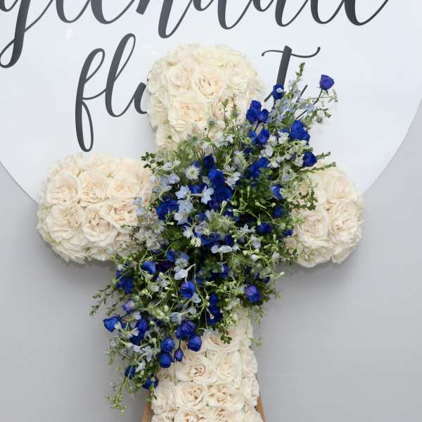 Cross-shaped floral arrangement with cream roses and blue flowers on an easel