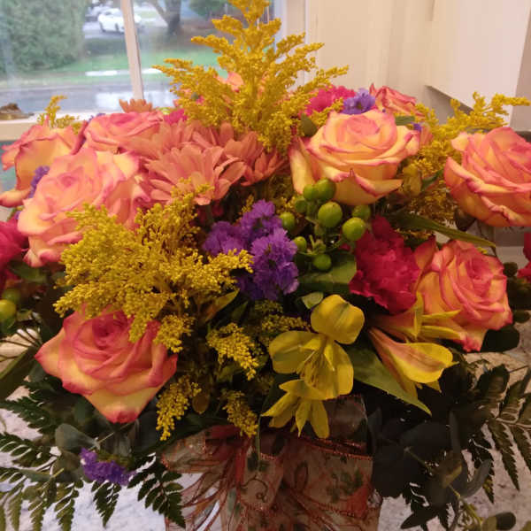 Bouquet of pink roses, yellow flowers, and purple accents in a glass vase