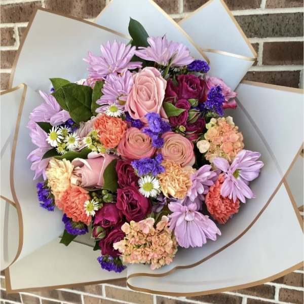 Mixed bouquet of pink, purple, and peach flowers wrapped in white paper
