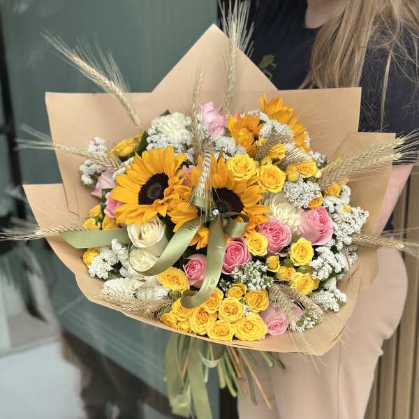 Bouquet of yellow sunflowers, pink and white roses, and dried grasses in kraft paper