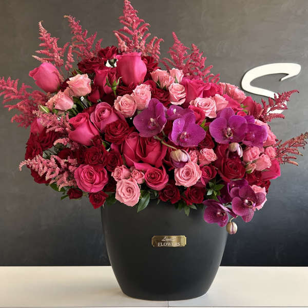 Pink and red rose arrangement with purple orchids in a black vase