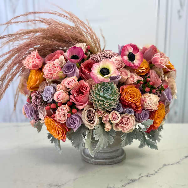 Mixed bouquet of pink, lavender, and orange flowers in a gray vase