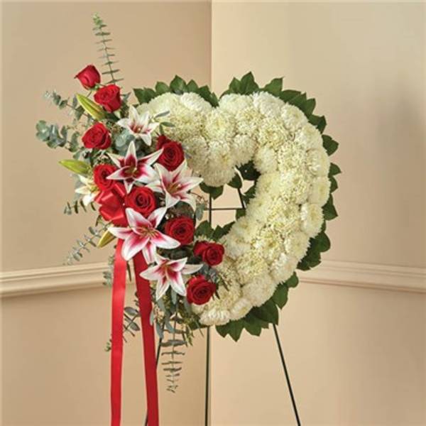 Heart-shaped floral wreath with white blooms and red roses on a stand