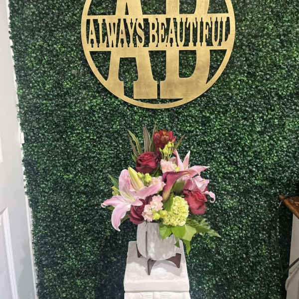 Pink lilies and roses arranged in a white vase on a pedestal