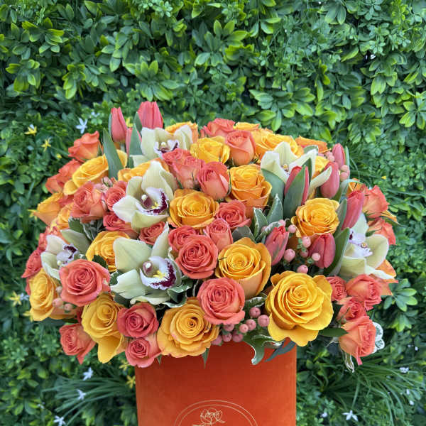 Orange hatbox arrangement of yellow and coral roses with orchids